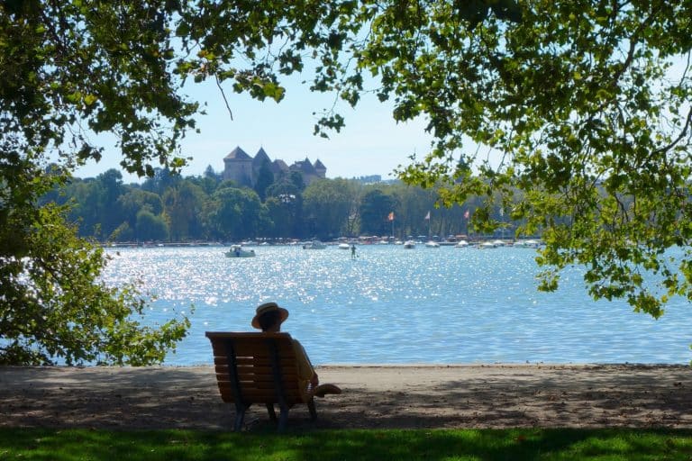 Personne assise face au lac sous arbres.